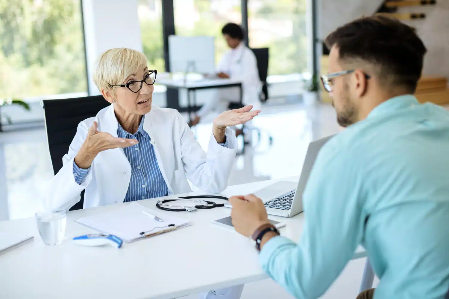 Doctor consulting with a patient in a modern dental office, discussing treatment options and insurance coverage, with a laptop and medical documents on the table.