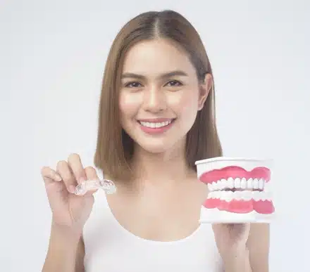 Woman holding clear aligner next to model of teeth, representing Invisalign treatment options at ARK Esthetics in Brooklyn.